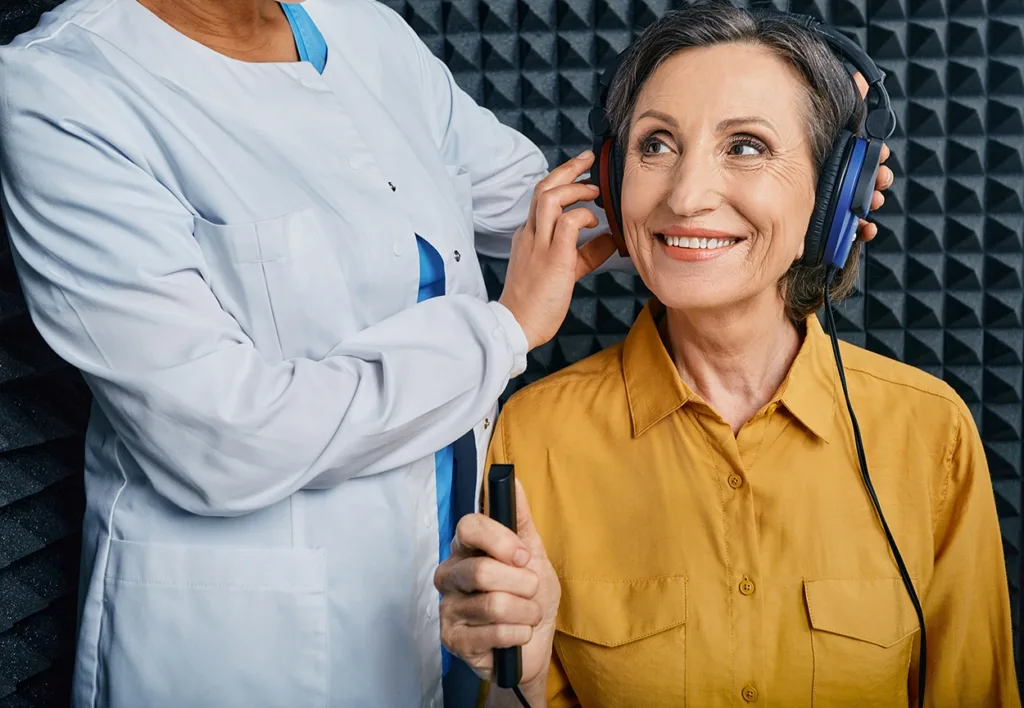 A senior woman at a hearing clinic in a soundproof audiometric booth using audiometry headphones and audiometer to get hearing tested